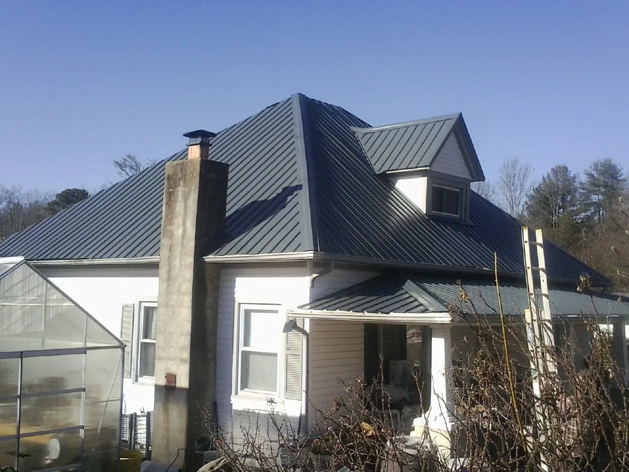 Dark blue standing seam metal roof on a white farmhouse with dormer — Slate & Tile Roof Repair by Roofing Brothers in Baring