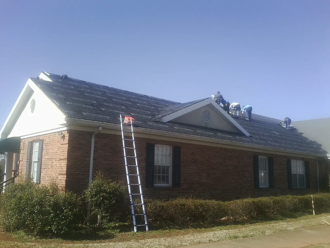 Crew tearing shingles off a brick ranch roof with a ladder set — Metal Roof Repair work by our crew in Baring
