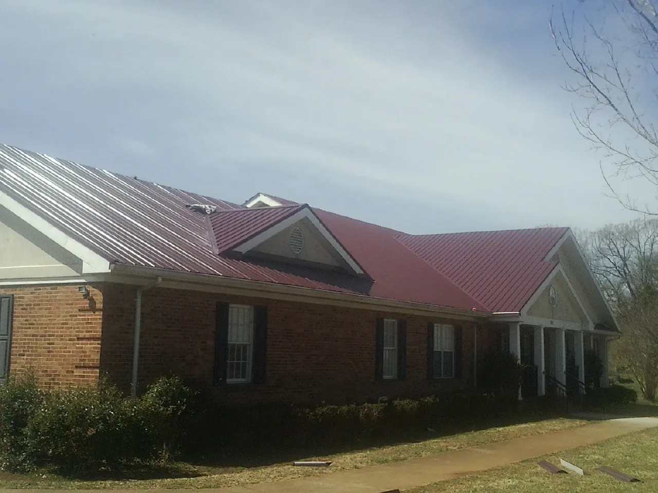 Red metal roof with gabled entries on a long brick building, from a Hail Damage Roof Repair job in Baring