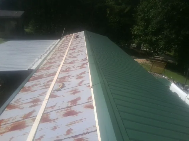 Old rusted panels beside newly installed green metal roofing — Wind Damage Roof Repair by Roofing Brothers in Baring