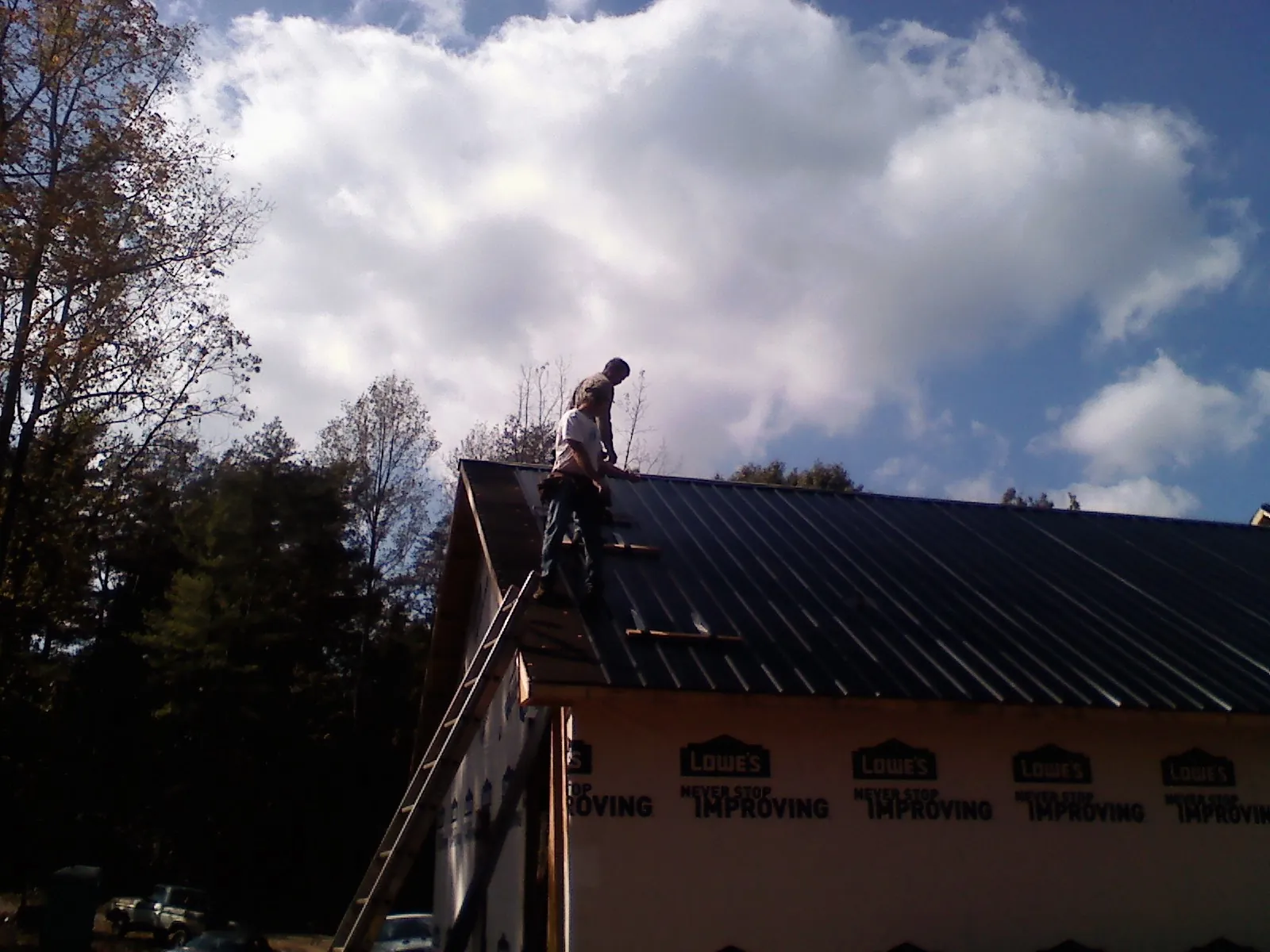 Roofer fastening dark metal panels high against a cloudy sky, from a Roof Inspection job in Baring