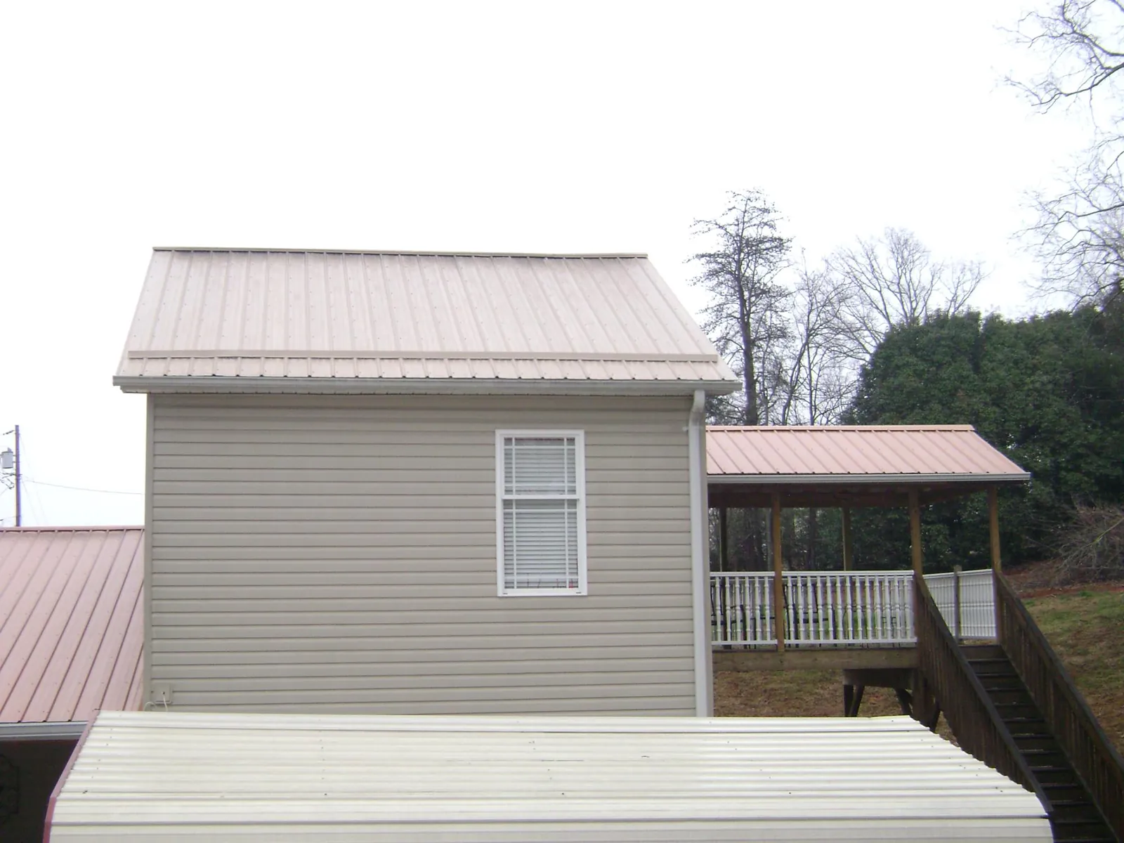 Tan metal roofs on a two story addition and attached porch, from a Roof Replacement job in Baring